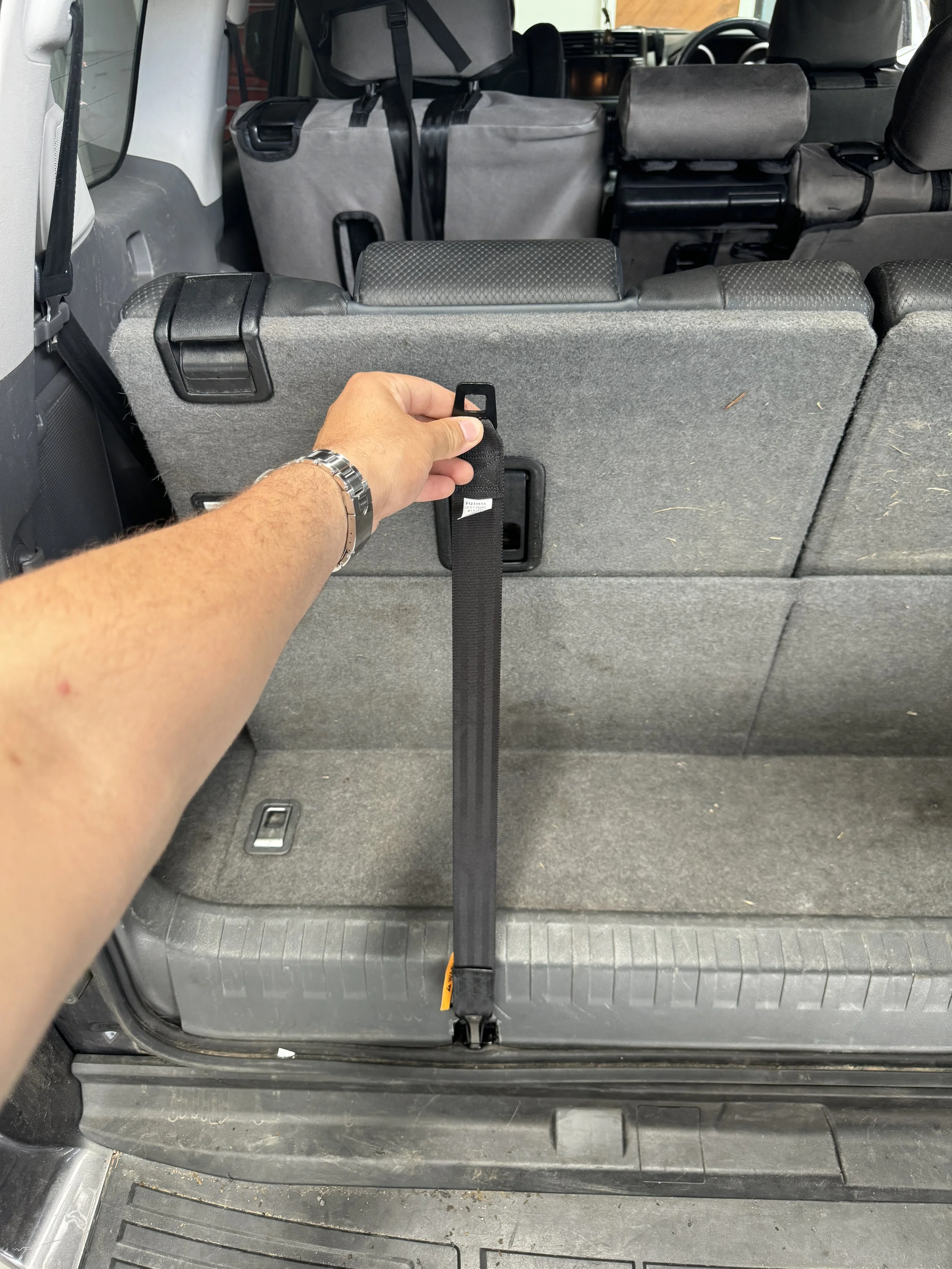 Person attaching a black seat belt to the back of a vehicle's third-row seat.