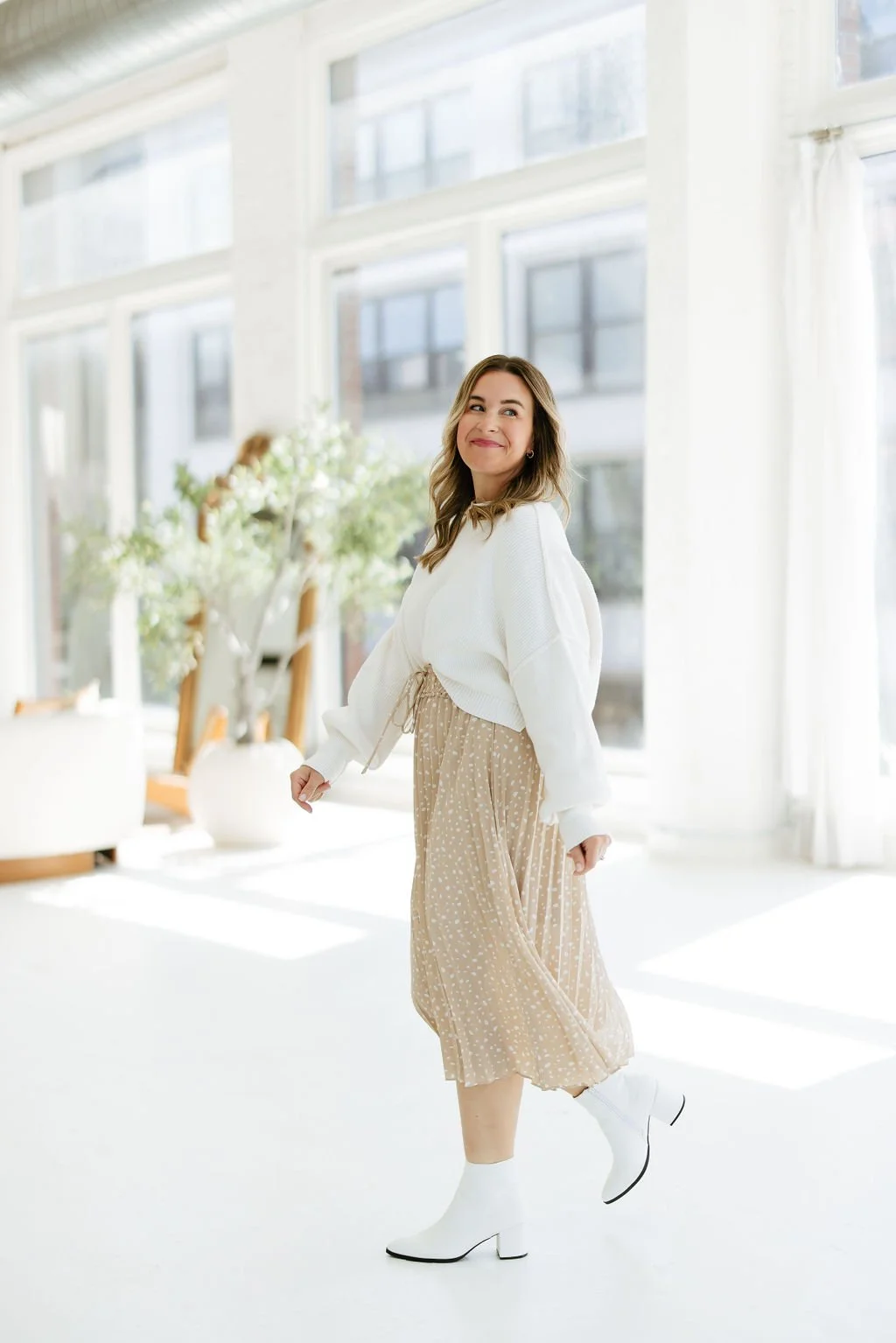 Kelly walks in a bright and airy space looking behind her.