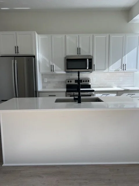 Modern kitchen with white cabinets, stainless steel refrigerator, microwave, stove, and a central island with a black faucet.