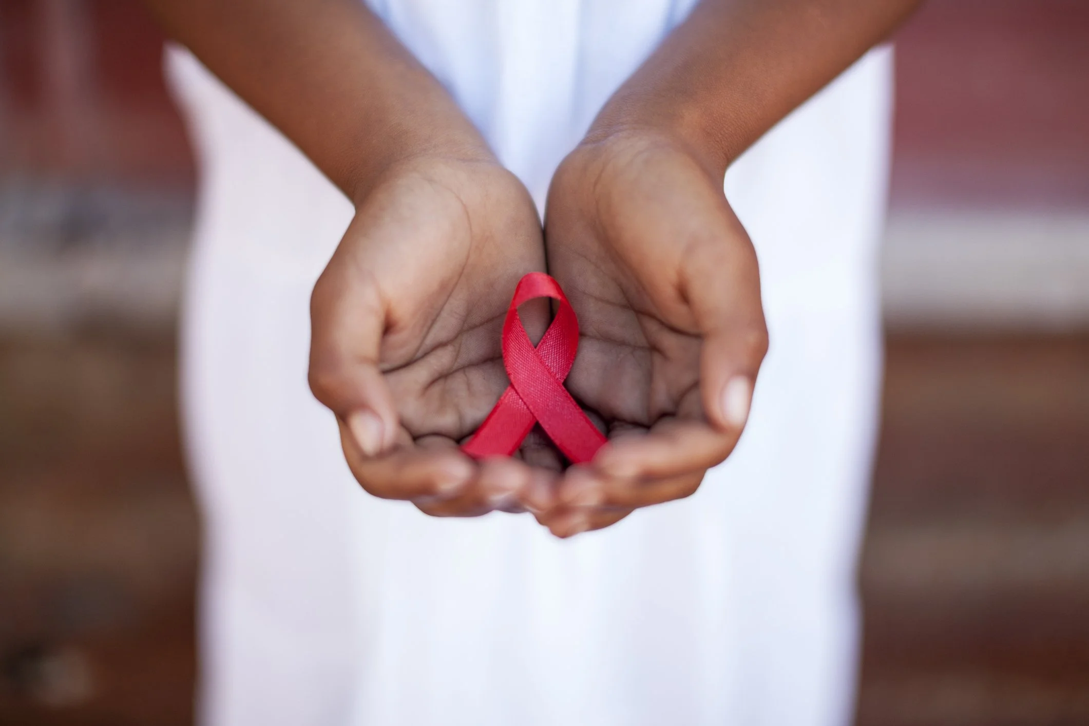 Mãos de pessoa segurando um laço vermelho, simbolizando a conscientização sobre HIV/AIDS.