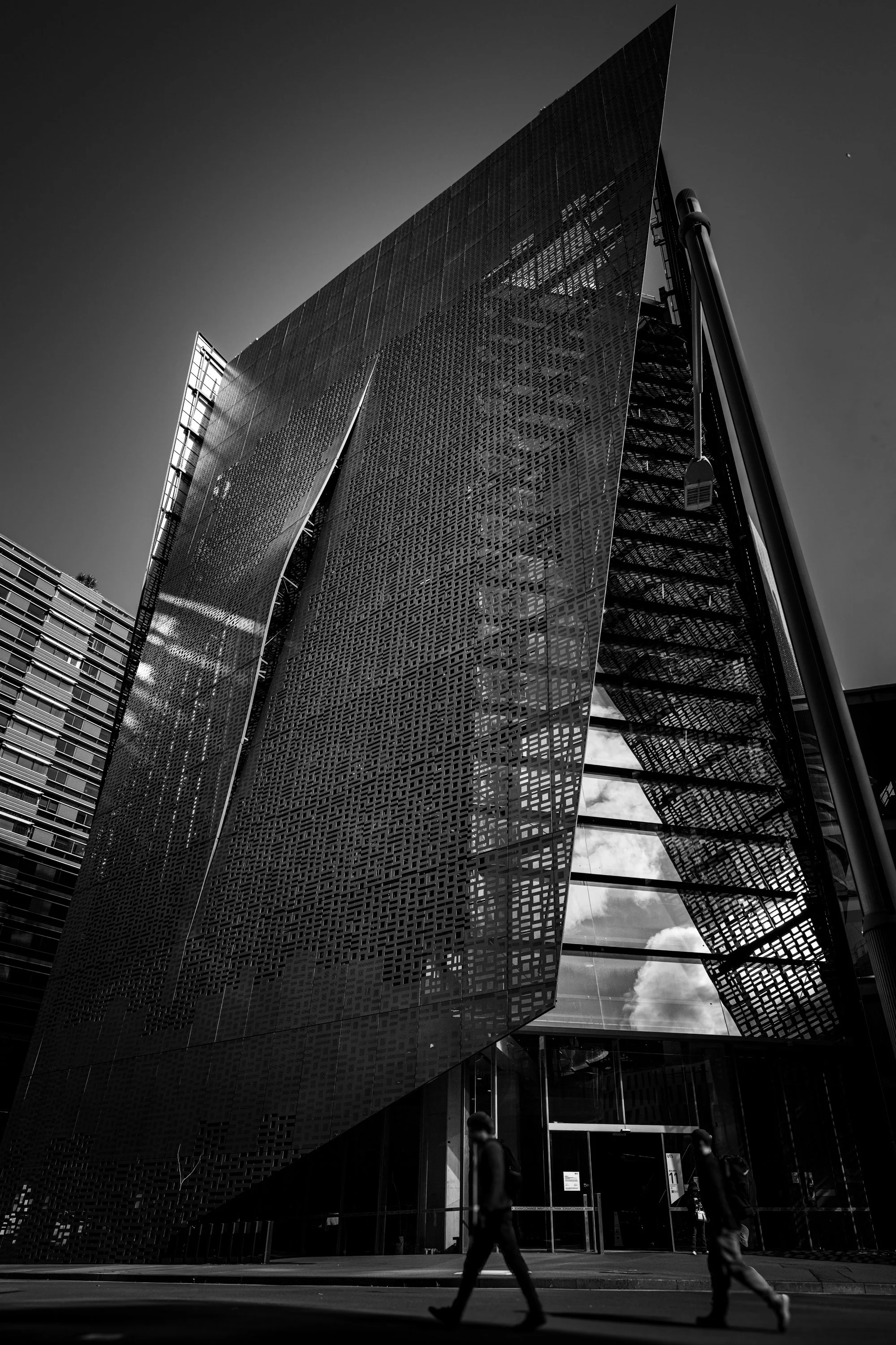 Black-and-white vertical architectural photograph of the UTS Faculty of Engineering and Information Technology Building, also known as Building 11 or the Broadway Building, in Sydney, Australia. Designed by Denton Corker Marshall, the building is sho