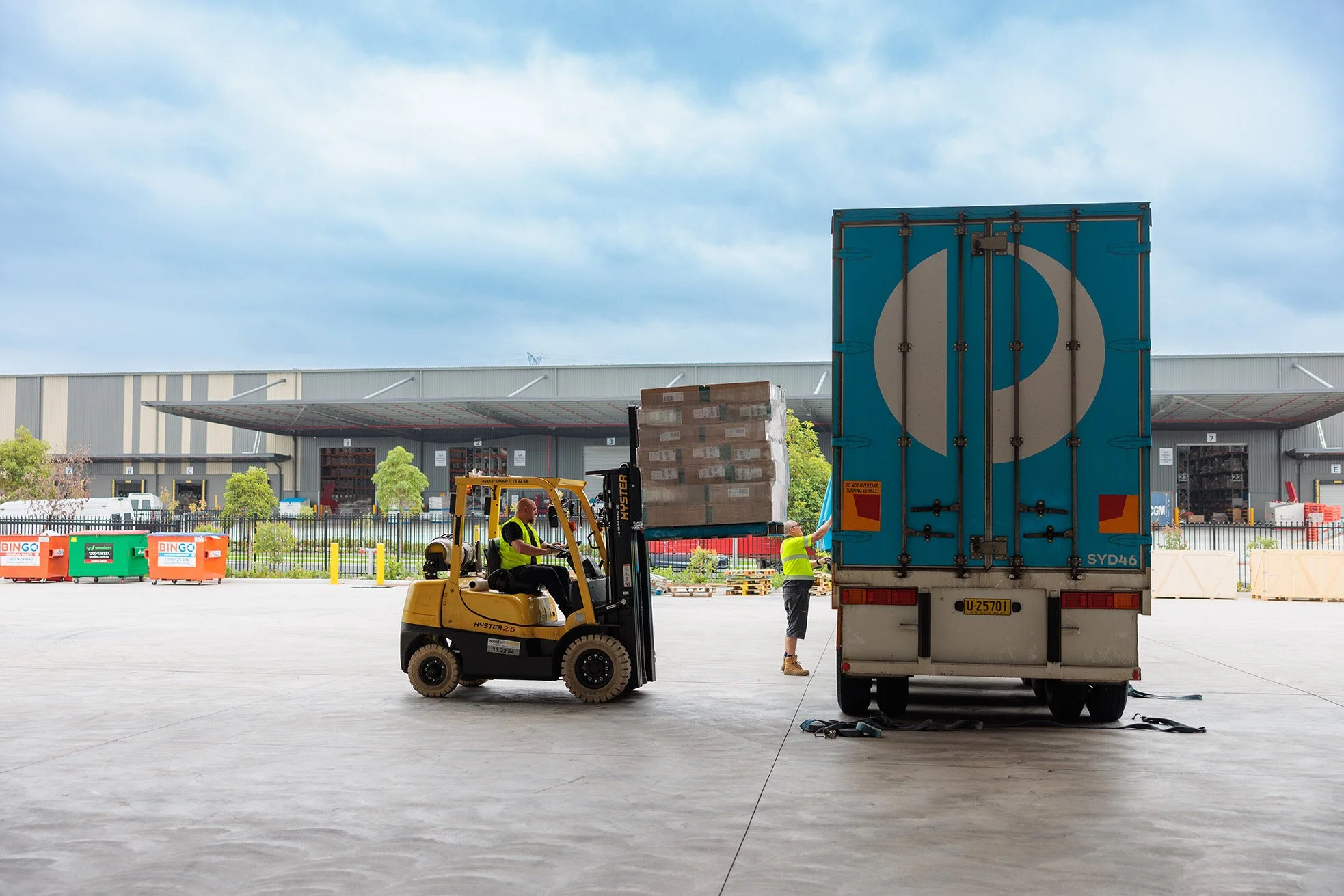 Workers at an industrial warehouse loading a truck with a forklift.