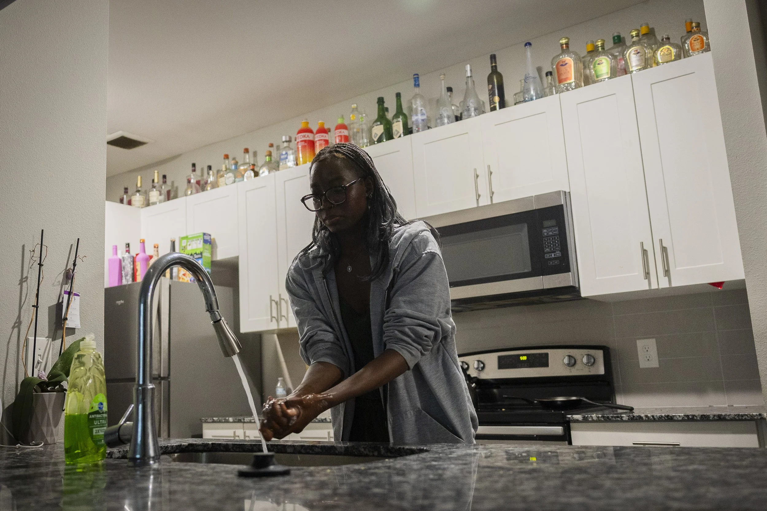 ALL THAT GLITTERS ISN’T GOLD: Junior Lola Popoola washes her hands among the dirty dishes and “bottle graveyard” left by her new roommates in their shared apartment in Denton on April 30. Popoola had to move to a different apartment complex to pay a 