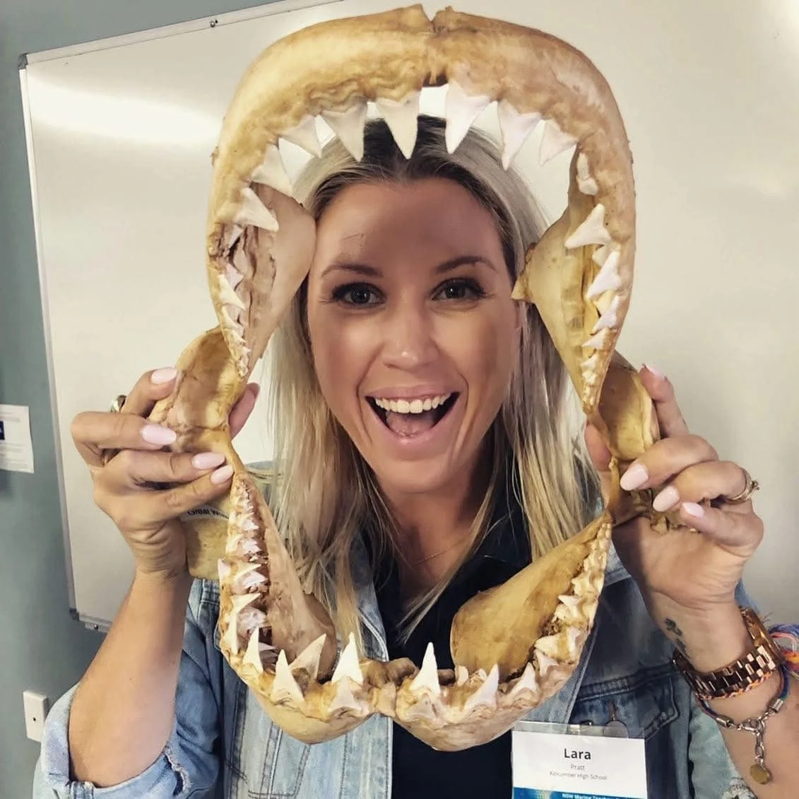 Woman holding a large shark jaw bone frame with teeth, smiling happily.
