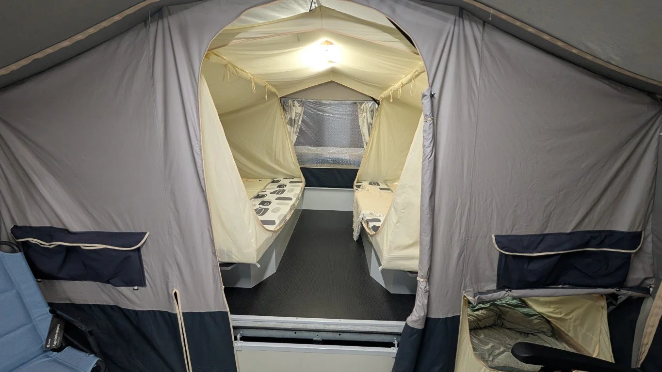 Inside of a gray camping tent with a view of the interior, showing two built-in beds with patterned bedding and a small window at the back.