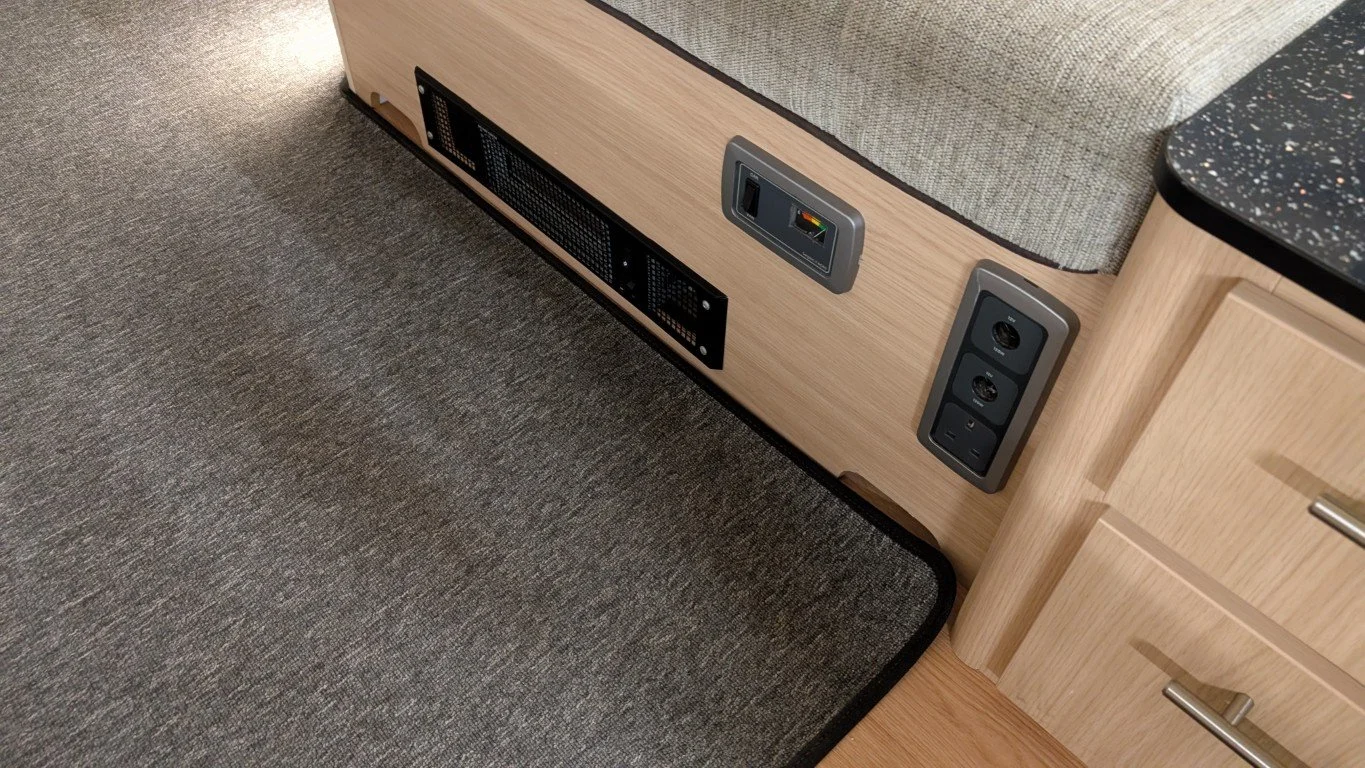 Close-up of a wooden panel with electrical outlets, USB ports, and ventilation vents next to a gray upholstered furniture piece and wooden cabinet with silver handles.