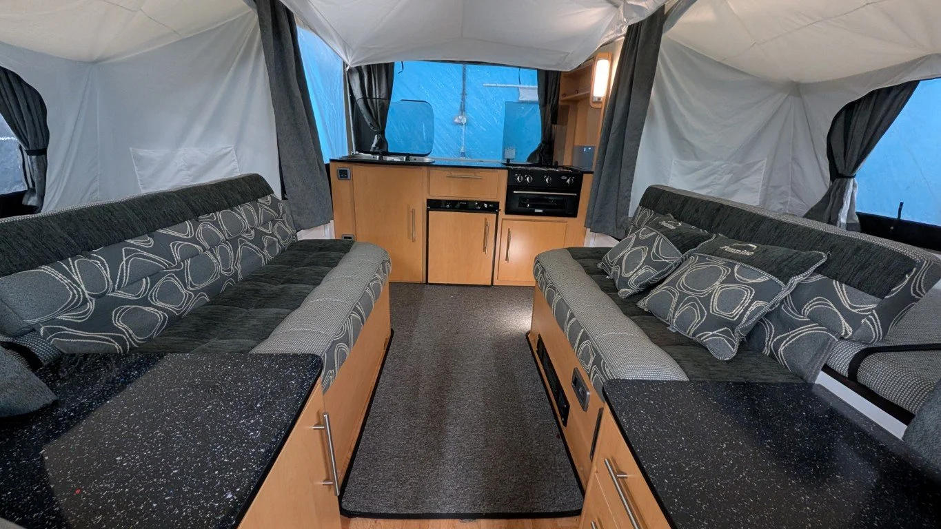 Interior of a tent with two long couches facing each other, black speckled countertops, and a small kitchenette with wooden cabinets, a stove, and a microwave.