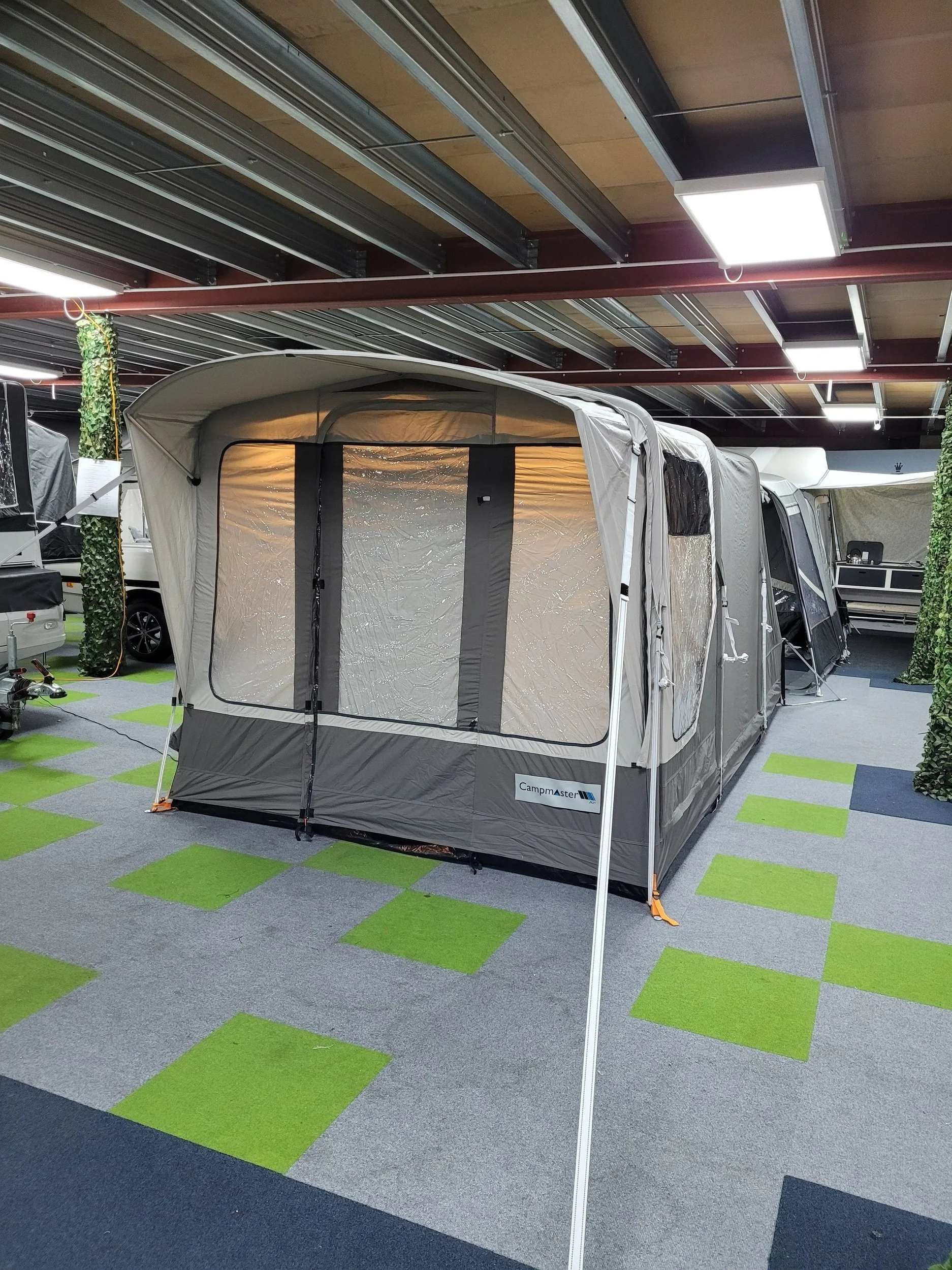 A Campamster Air set up indoors in a store, with a gray and black design, brand name 'CampMaster', and green and gray carpet tiles on the floor.