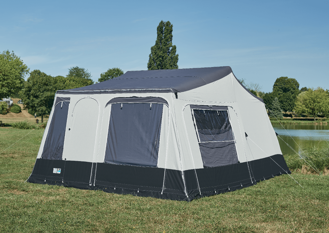 A large outdoor Jamet camping tent set up on grass near a body of water with trees in the background.