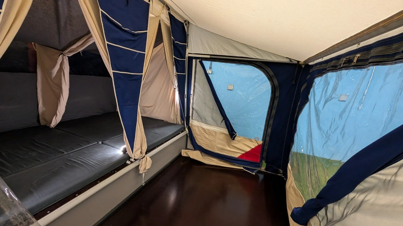 Interior of a camping tent with beds and windows.