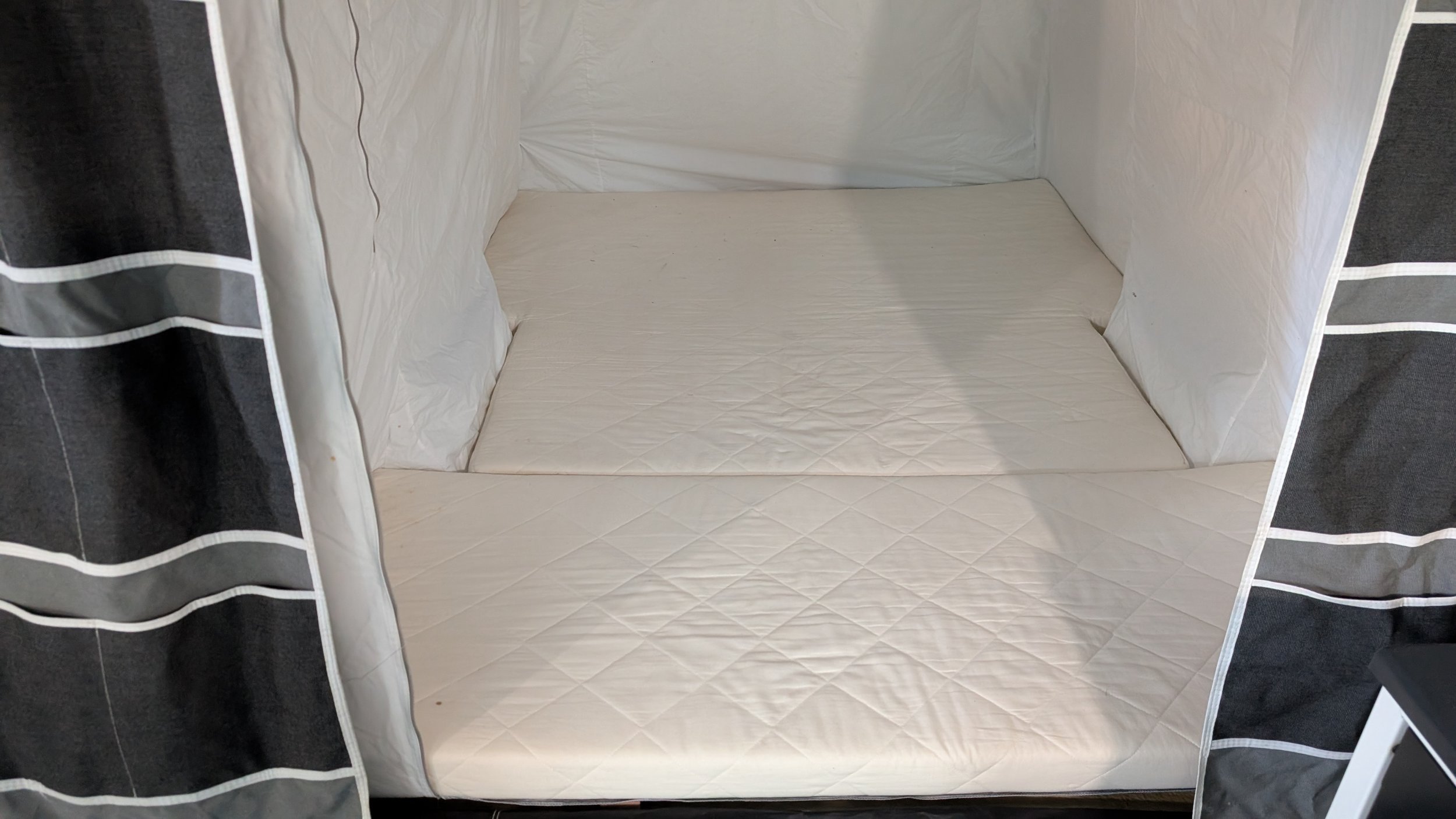 Open tent with striped black and white curtains, showing a white mattress inside.