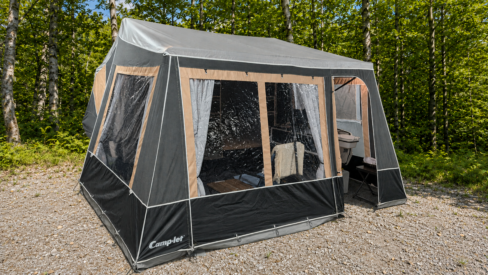 A black and beige camping tent set up outdoors on rocky ground with green trees in the background. The tent has transparent plastic windows and a side entrance, with interior visible through the windows.