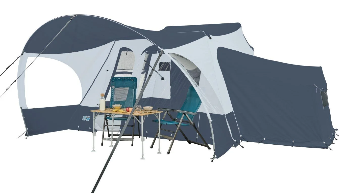 A large, dark blue and white Jamet Compact camping tent with an extended canopy and two camping chairs, with a small table set with a bottle, apples, bananas, and a bowl, against a plain white background.