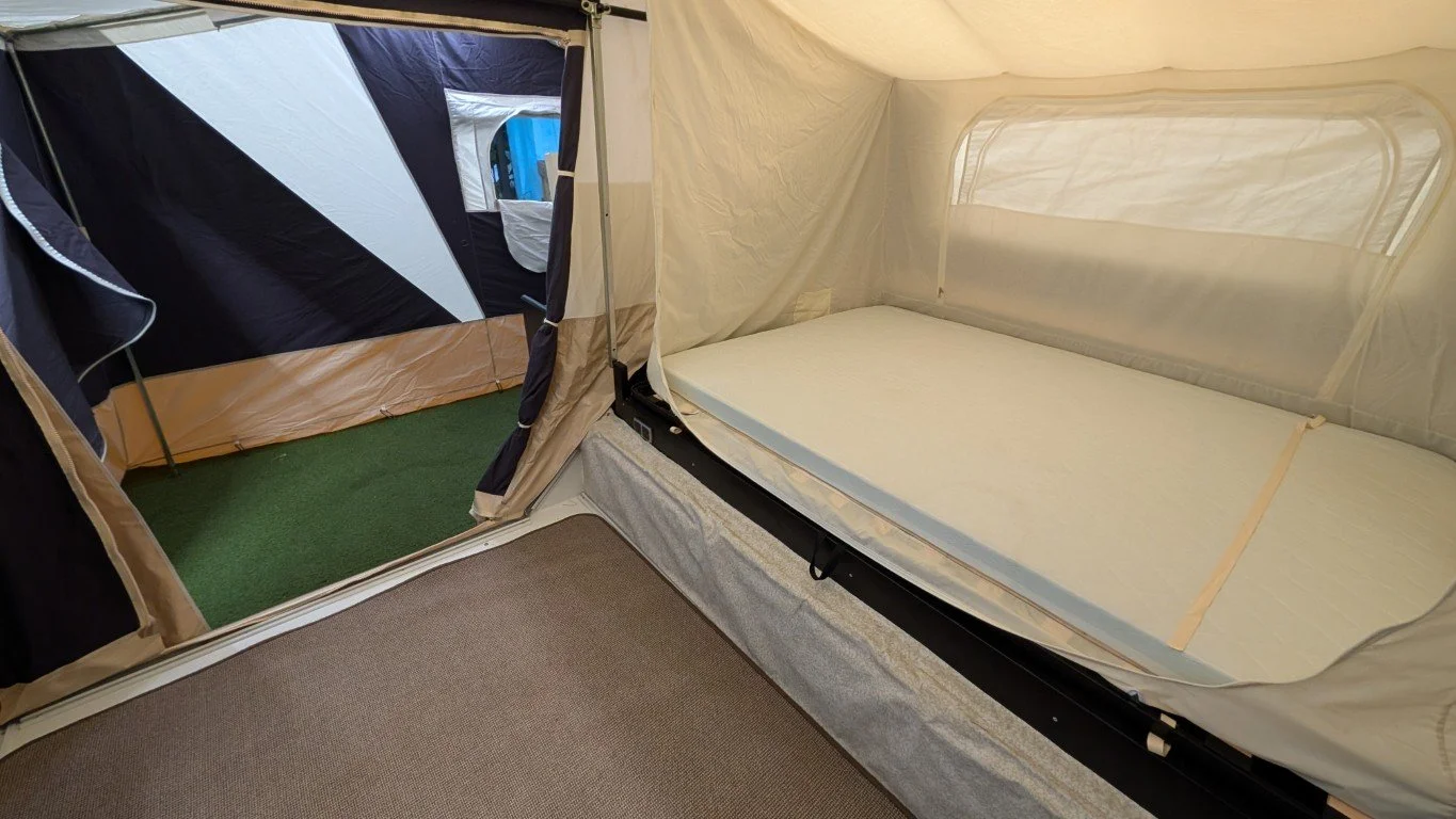 Inside a pop-up camper with a bed on the right side and an attached tent area with a door on the left side.