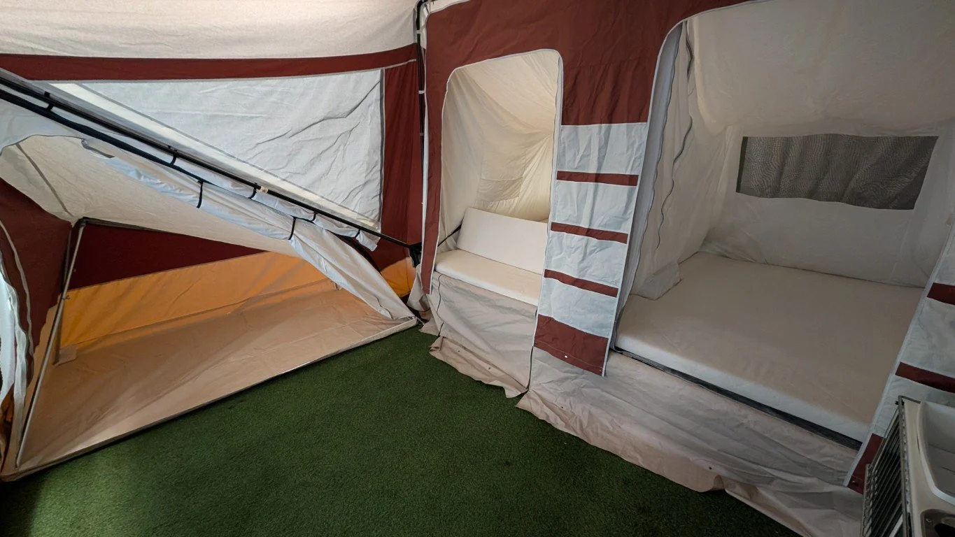 A camping tent with an attached screened-in sleeping area and a small bubble-like room, set up on green artificial grass.