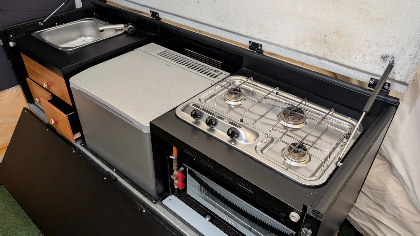Compact kitchen unit with stainless steel sink, portable stove with three burners, small oven, and drawers.