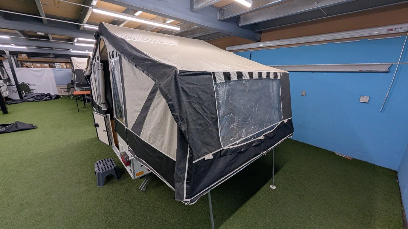 A pop-up camper trailer indoors on a green artificial turf floor.