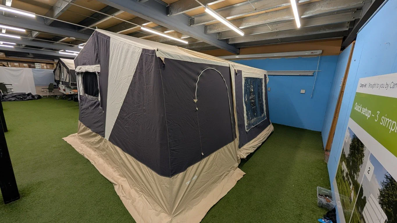 A large camping tent set up indoors with artificial grass flooring and blue walls, with one window and a doorway, in a display or store setting.