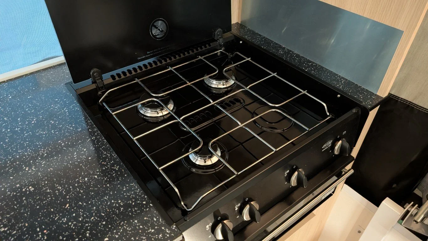 black gas stove with four burners and control knobs on the front, set in a speckled black kitchen countertop.