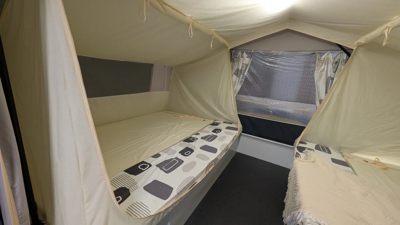 Interior of a small tent with sleeping areas on both sides and a window with curtains in the back.