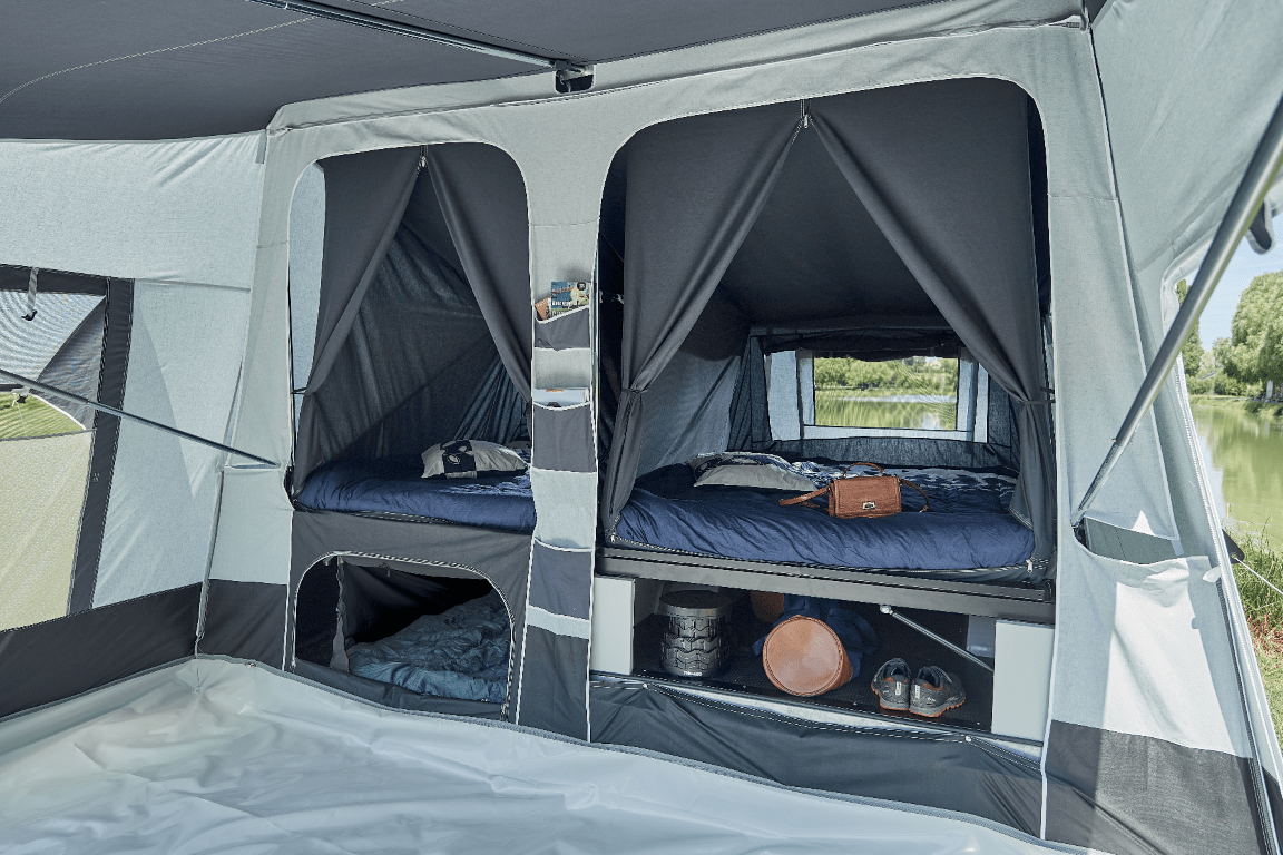 Inside view of a canvas Jamet camping tent with two elevated sleeping areas, storage compartments, and outdoor scenery visible through a window.