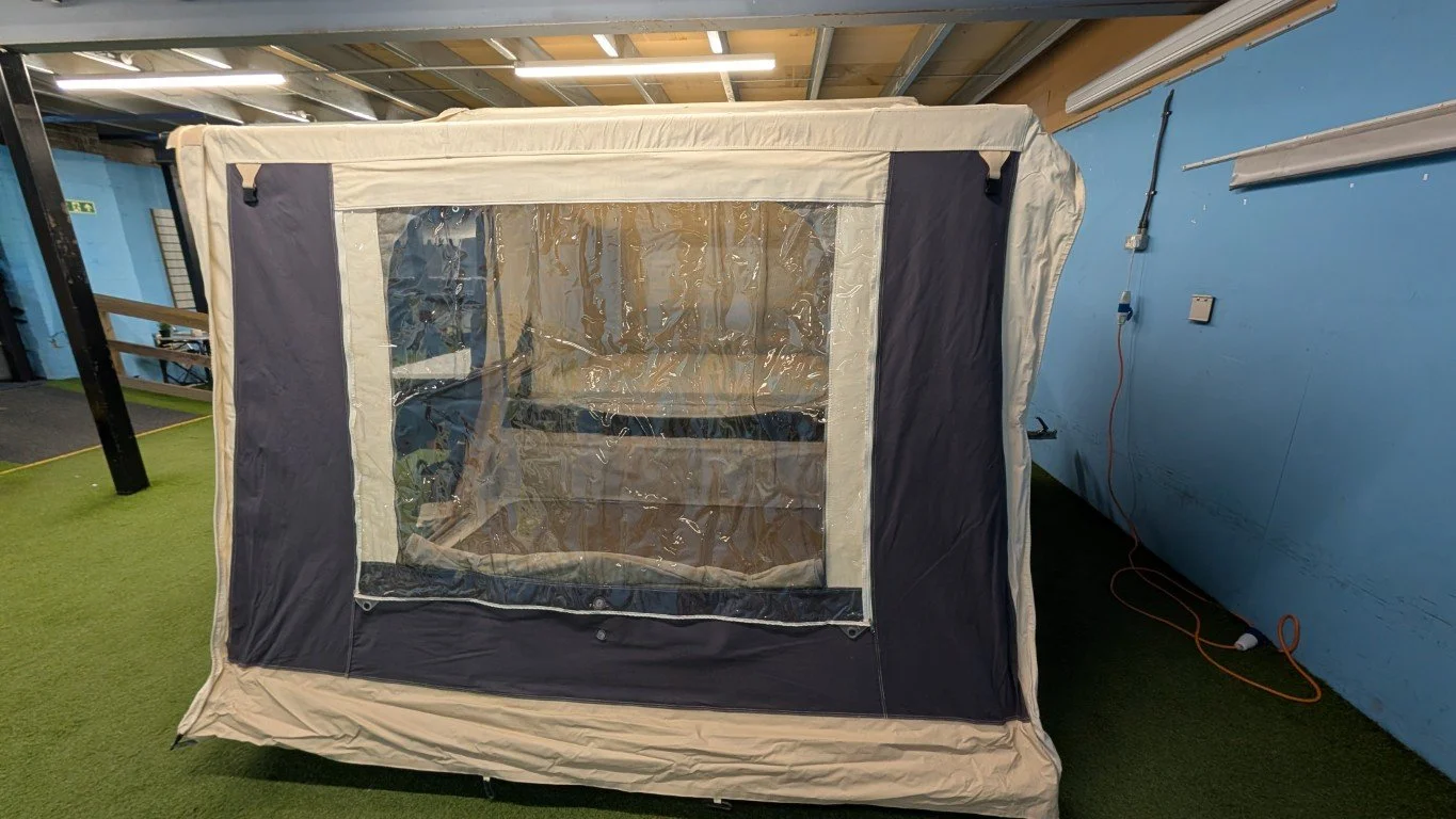 A beige and black pop-up tent with clear plastic windows inside a room with blue walls and artificial grass flooring.