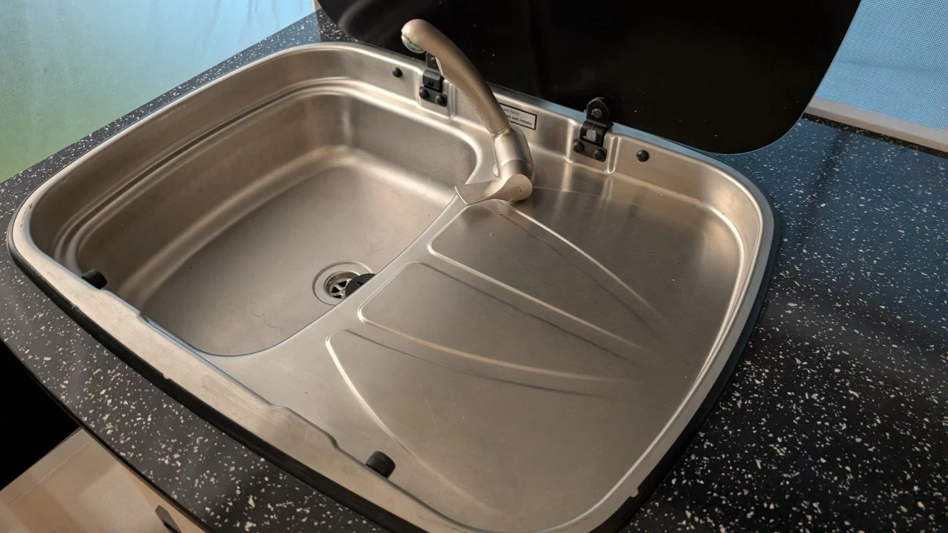 A stainless steel kitchen sink with an attached faucet, set into a black speckled countertop, with the sink cover lifted open.