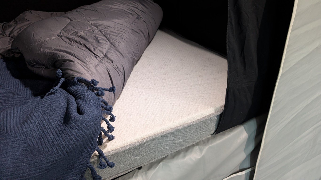 Empty bed with a pillow and blanket inside a teal-colored sleeping pod.