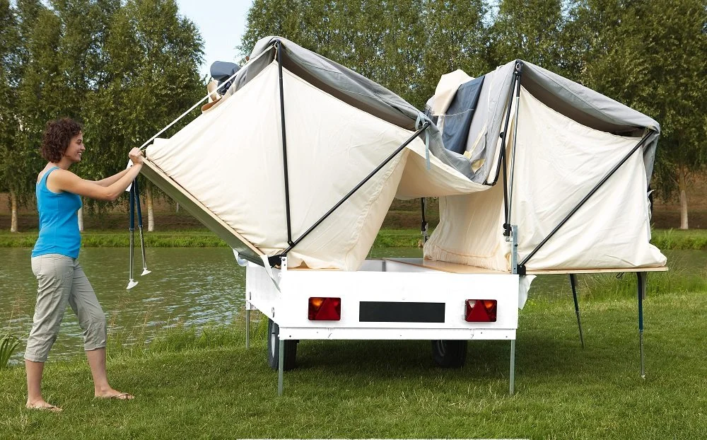 Woman setting up a Camplair  trailer near a lake with trees in the background.