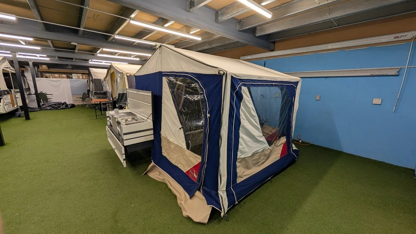 Indoor display of camping tents and outdoor gear on green artificial turf.