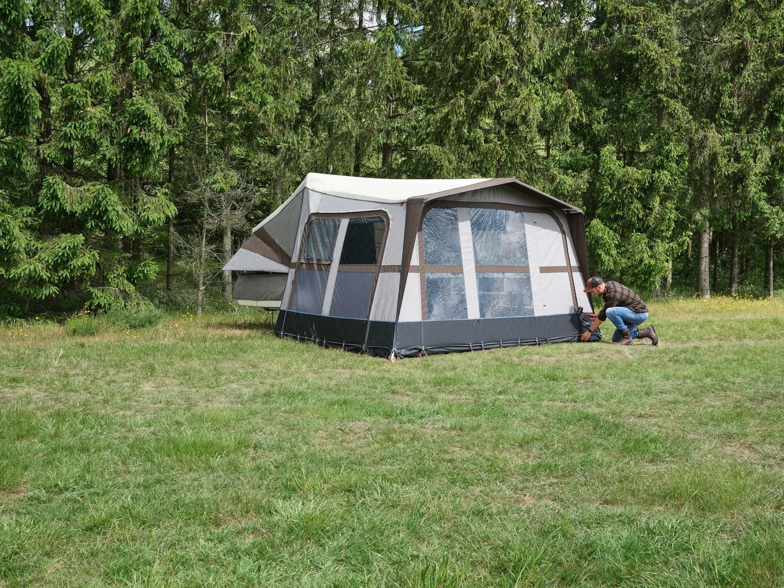 Man kneeling next to a Camp-let  tent on a grassy area near a forest.