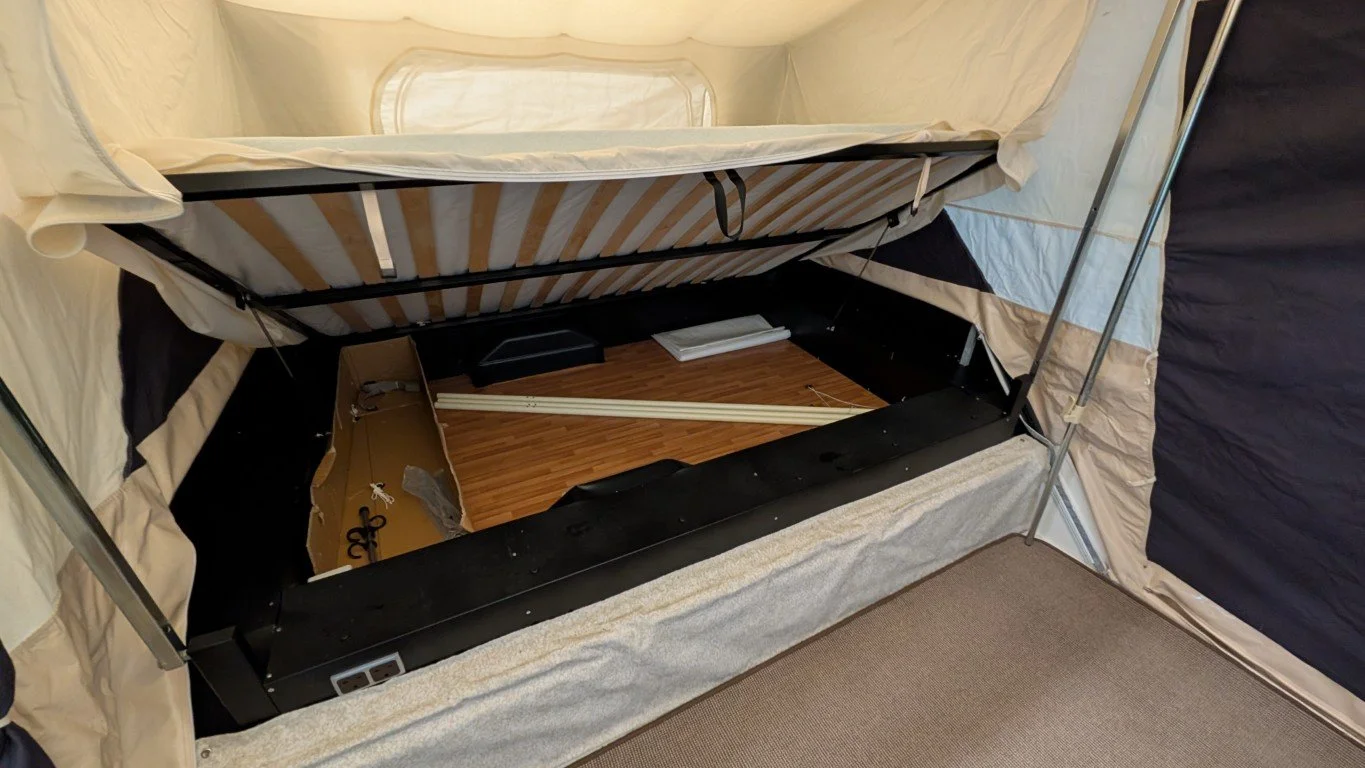 Interior of a tent with a raised bed, some scattered parts, and a wooden floor.