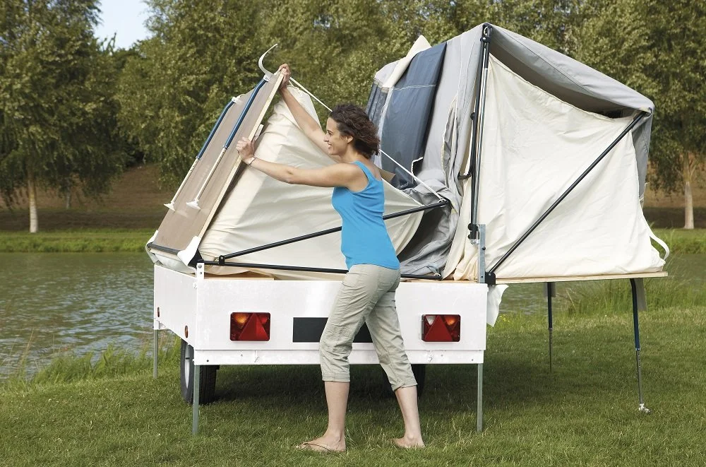 A woman setting up a Camplair camper near a lake in a park.