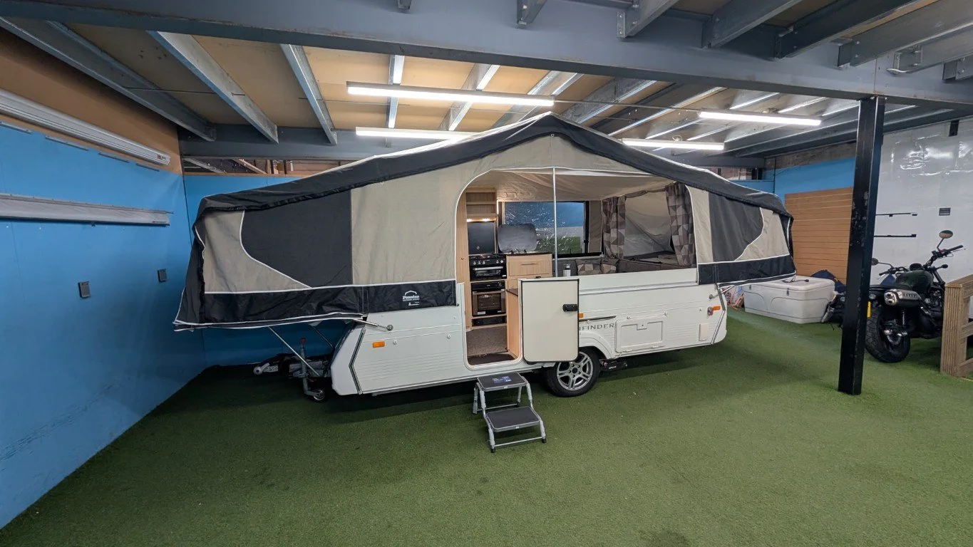 A small camper trailer with an extended pop-up tent, set inside a storage or display warehouse.