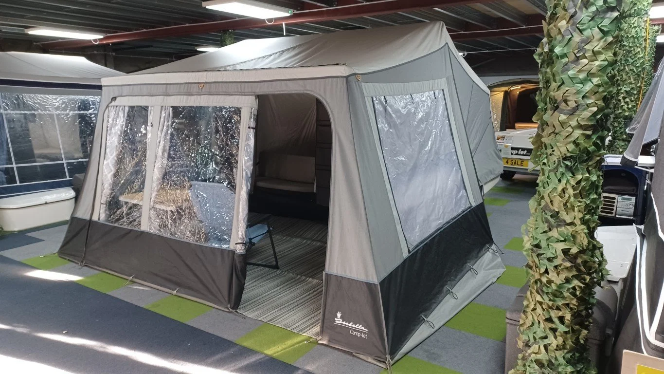 Camp-let Trailer Tent with transparent windows set up indoors in a showroom, with other camping and RV equipment nearby.