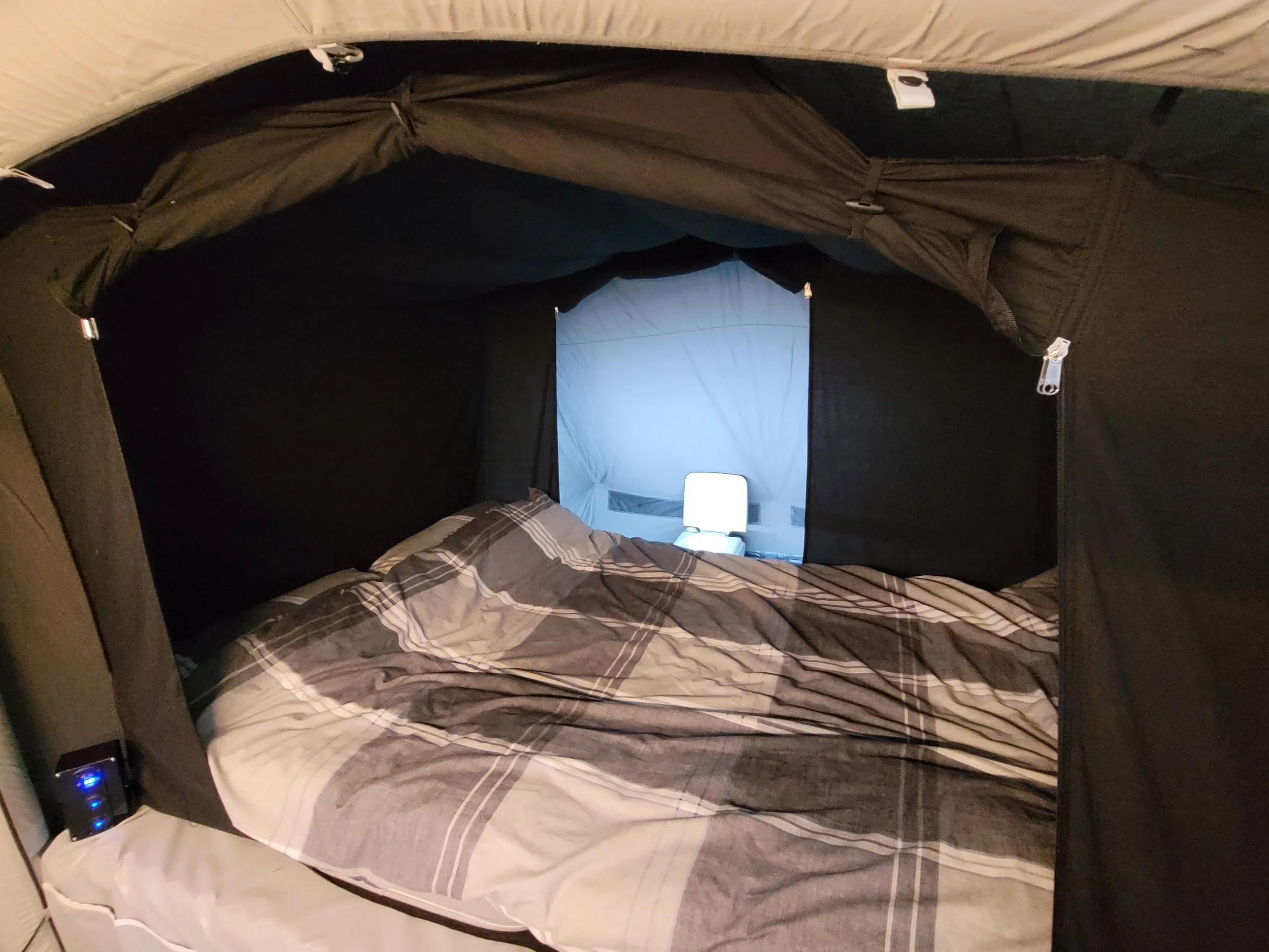 Interior of a Campmaster Air with a filled bed and a window showing a blue screen and a portable device with blue lights inside a room