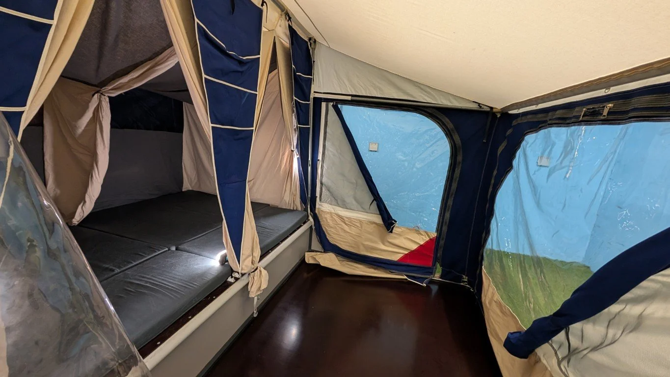 Interior of a tent with a sleeping area and windows showing outdoor landscape.