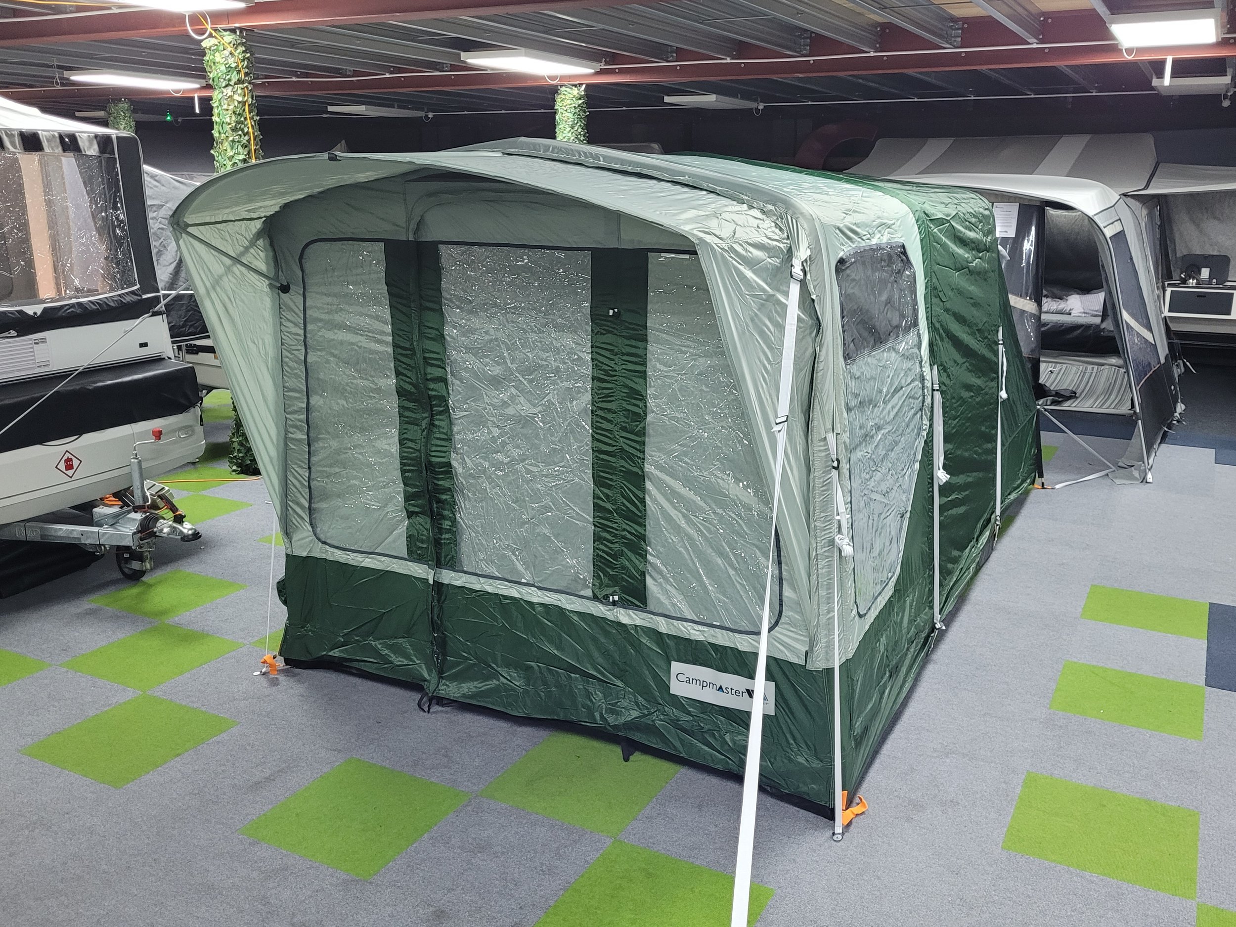 Campmaster Air A green and gray CampMaster portable camping tent on display indoors, with other camping equipment and tents visible in the background.