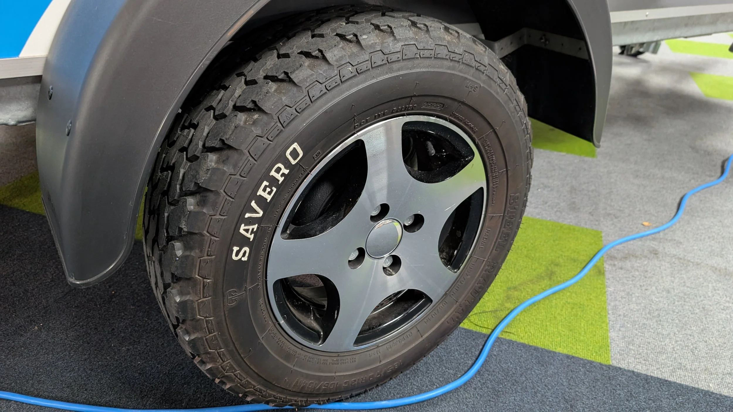 A close-up of a vehicle tire and alloy wheel on a black and green mat with a blue cable nearby.