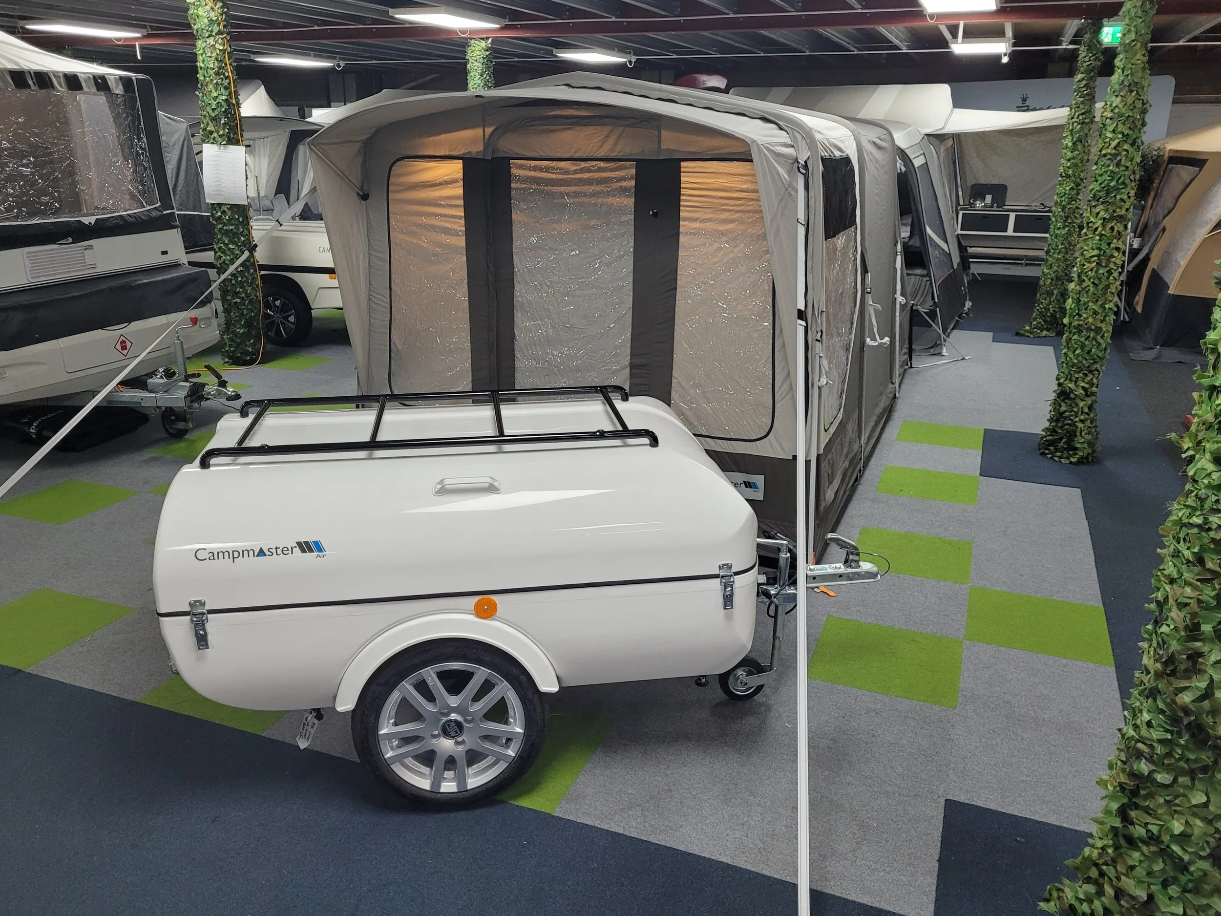 Campmaster Air trailer with a black roof rack, parked indoors among other camper trailers and caravans, with a fold-out tent extension attached.