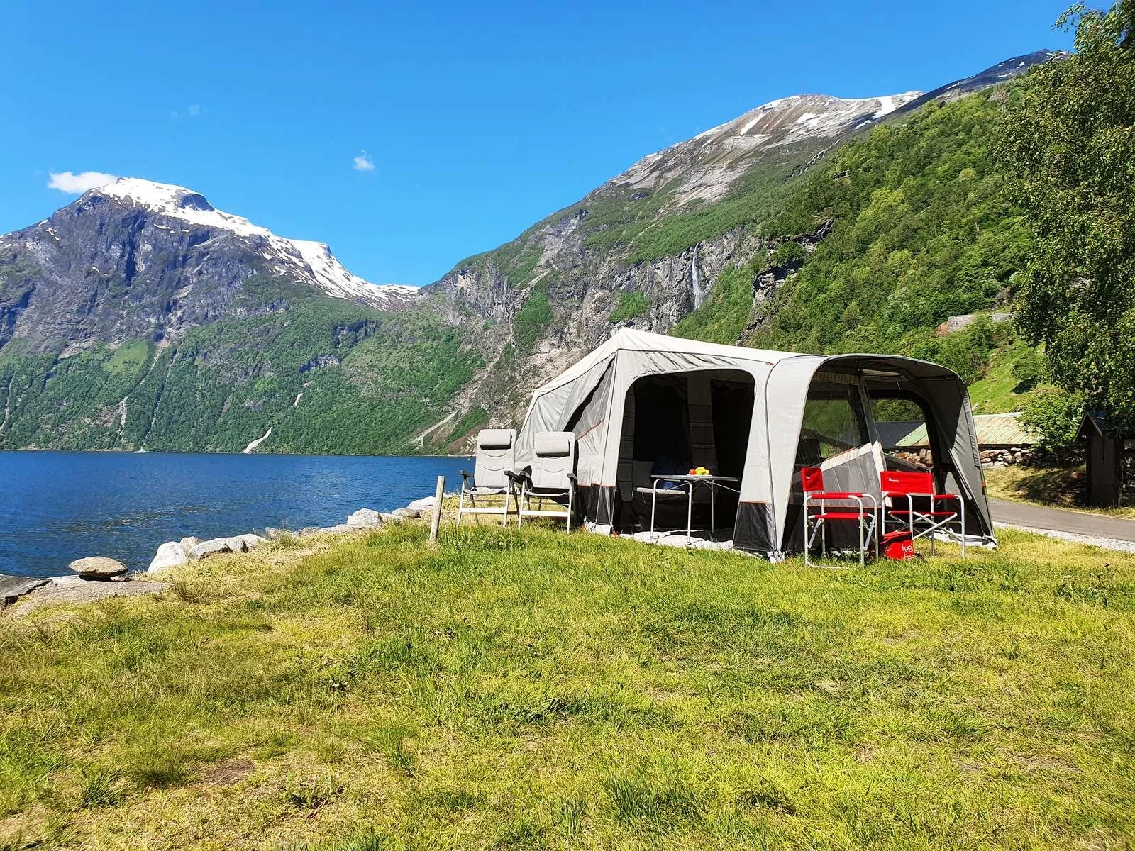 Camp-let tent set up on grassy lakeside with mountains and a blue sky in the background.
