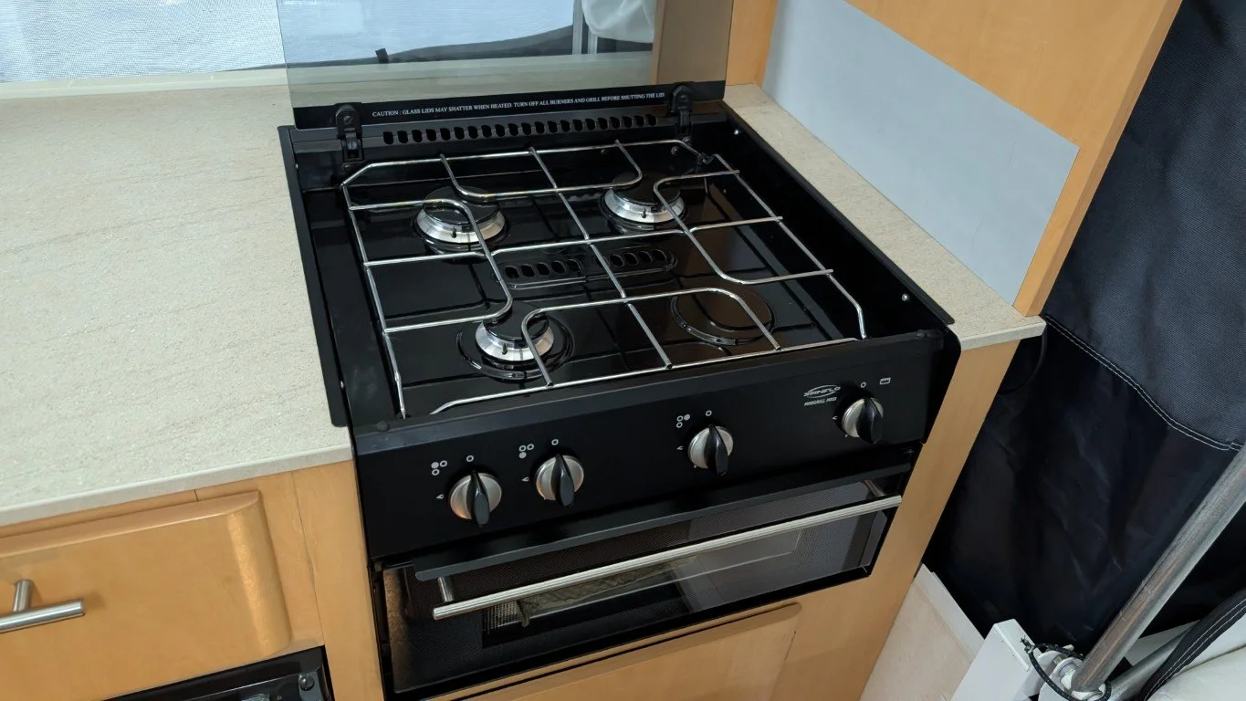 A black gas stove with four burners, control knobs, and an oven in a kitchen setting surrounded by wooden cabinetry and a beige countertop.