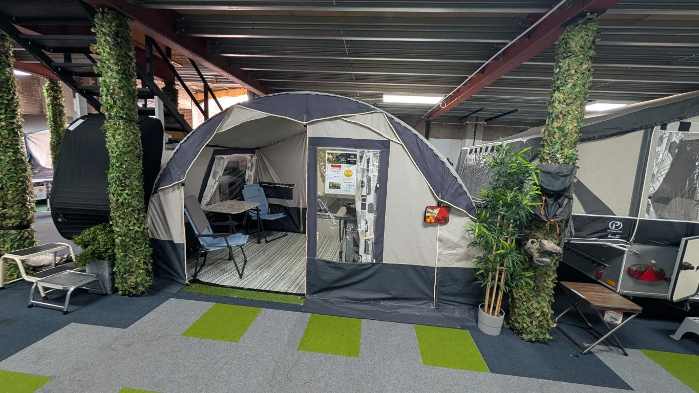 Indoor displays of RV tents with outdoor furniture and greenery in a showroom.