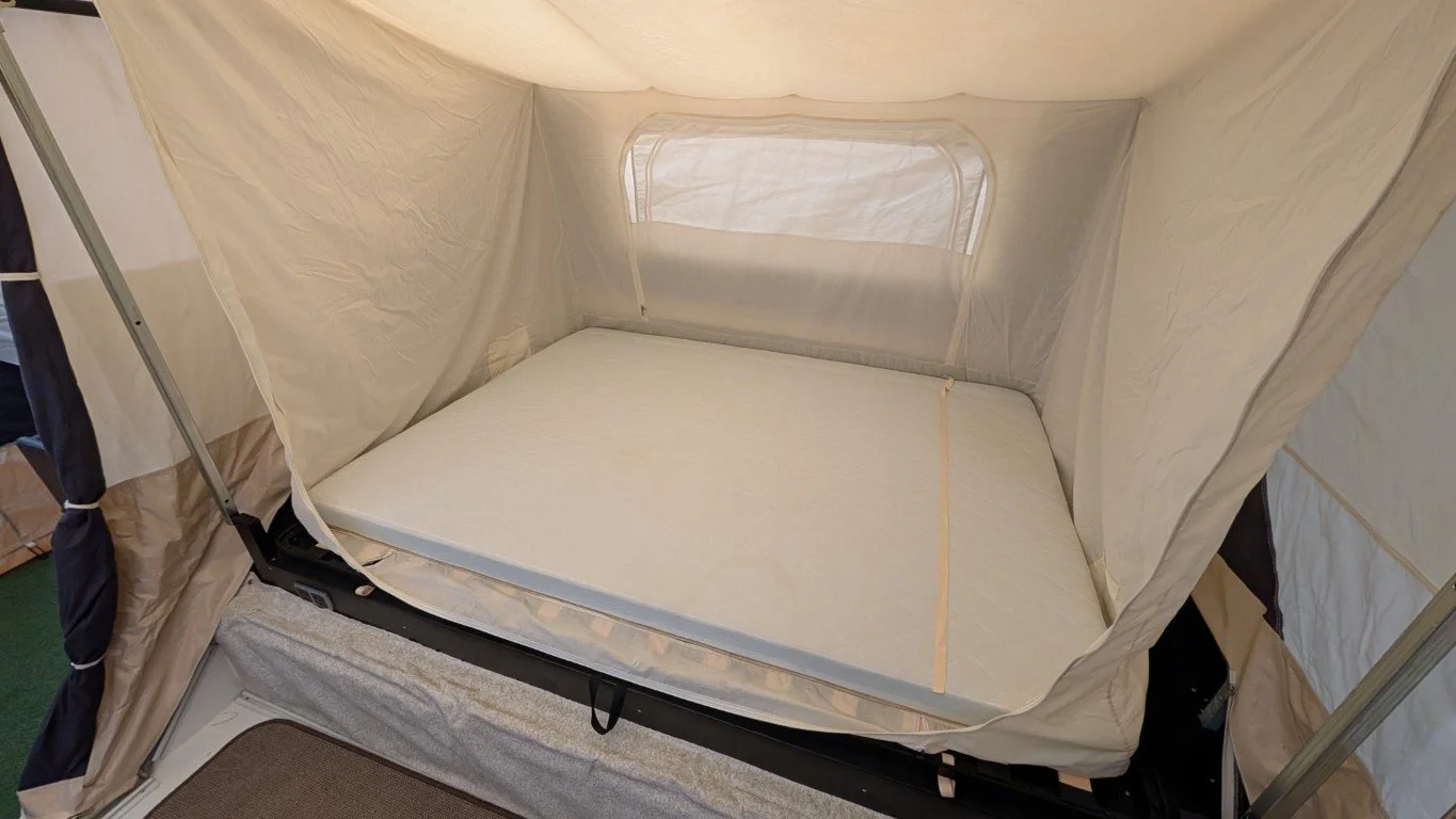 Inside a beige pop-up camper tent with a mattress, window, and fabric walls.