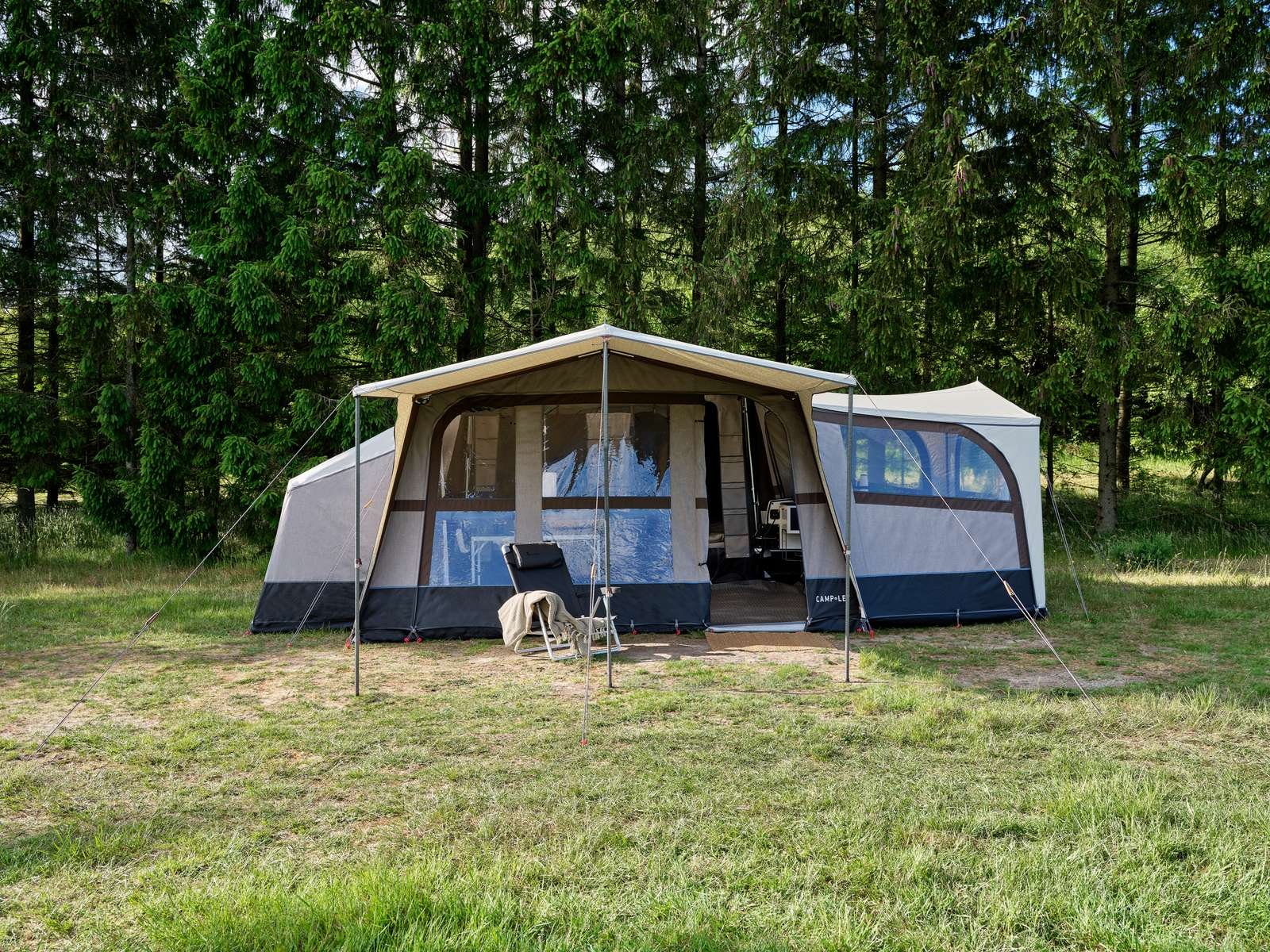 Camp-let tent set up on a grassy field with a forest background and outdoor chair outside the entrance.