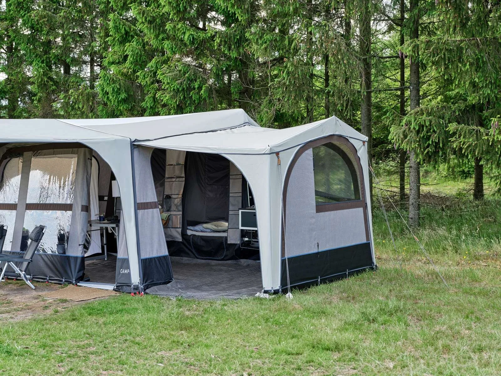 A large gray and black camping tent set up in a grassy area with trees in the background.