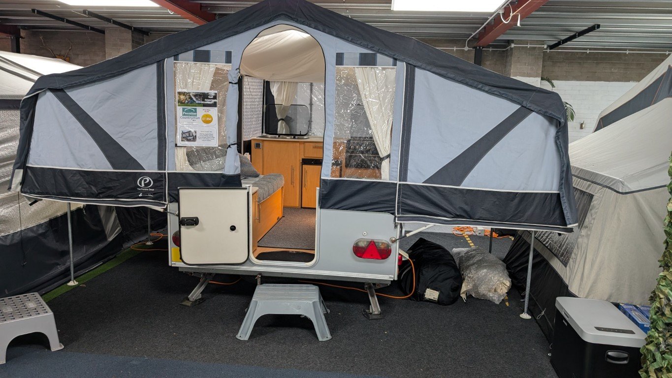 A small travel trailer with an expandable tent section at a dealership or showroom.