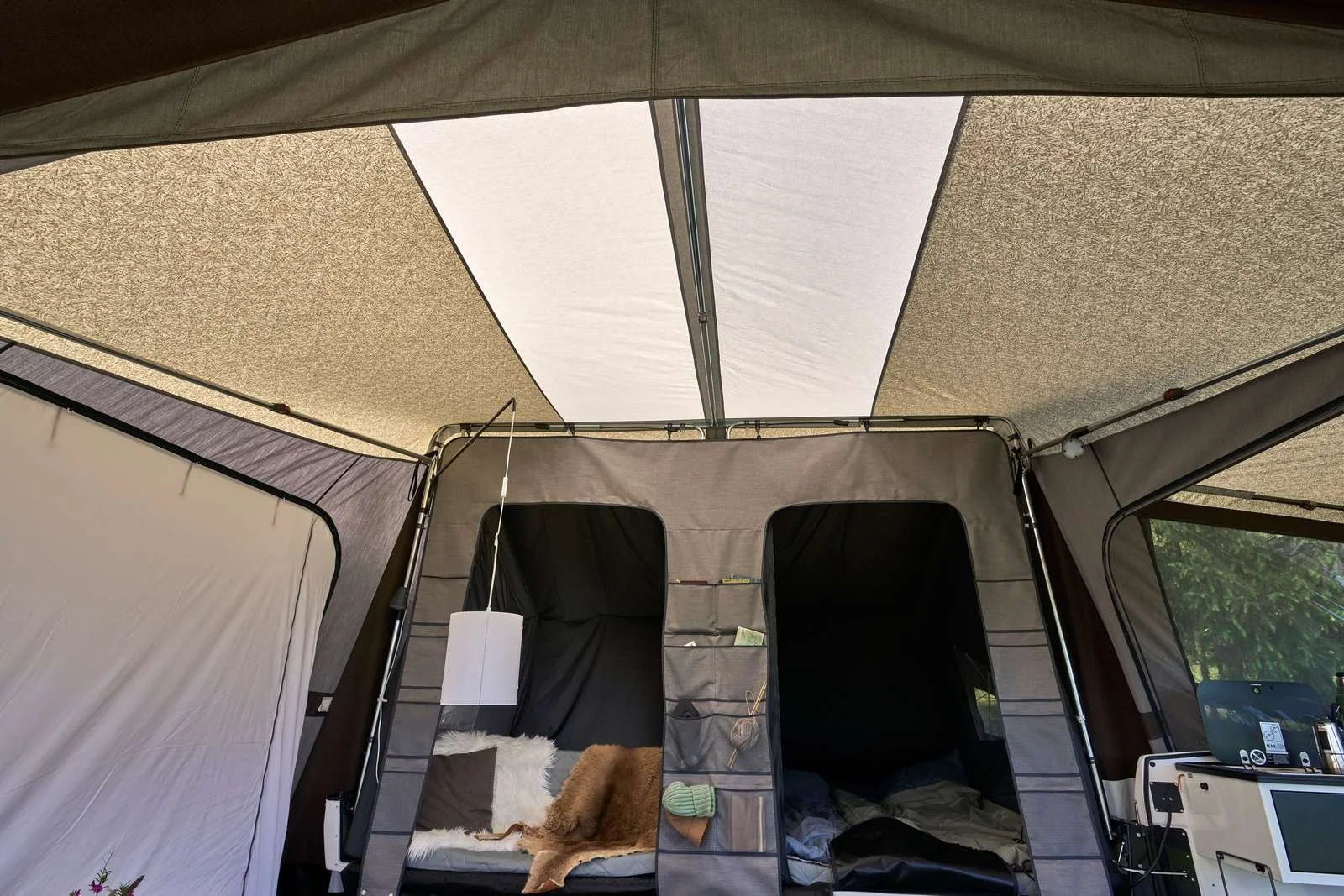 Inside a camping tent with two sections, pillows, a blanket, and a small hanging light.