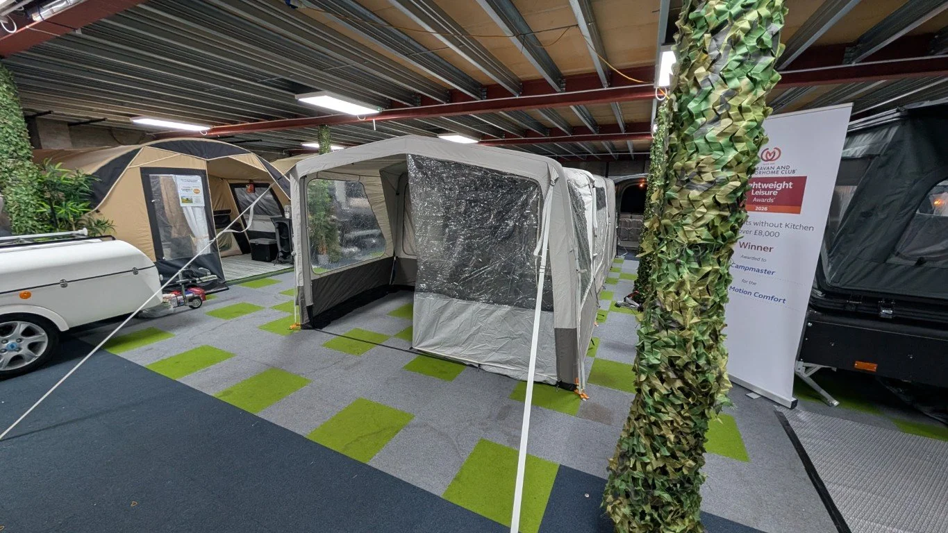 Indoor display of camping equipment including tents, a caravan trailer, and a promotional sign in a showroom.