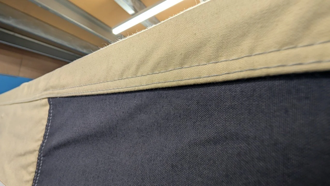 Close-up of a fabric surface with black and tan sections, taken indoors under bright lighting, showing detailed stitching.